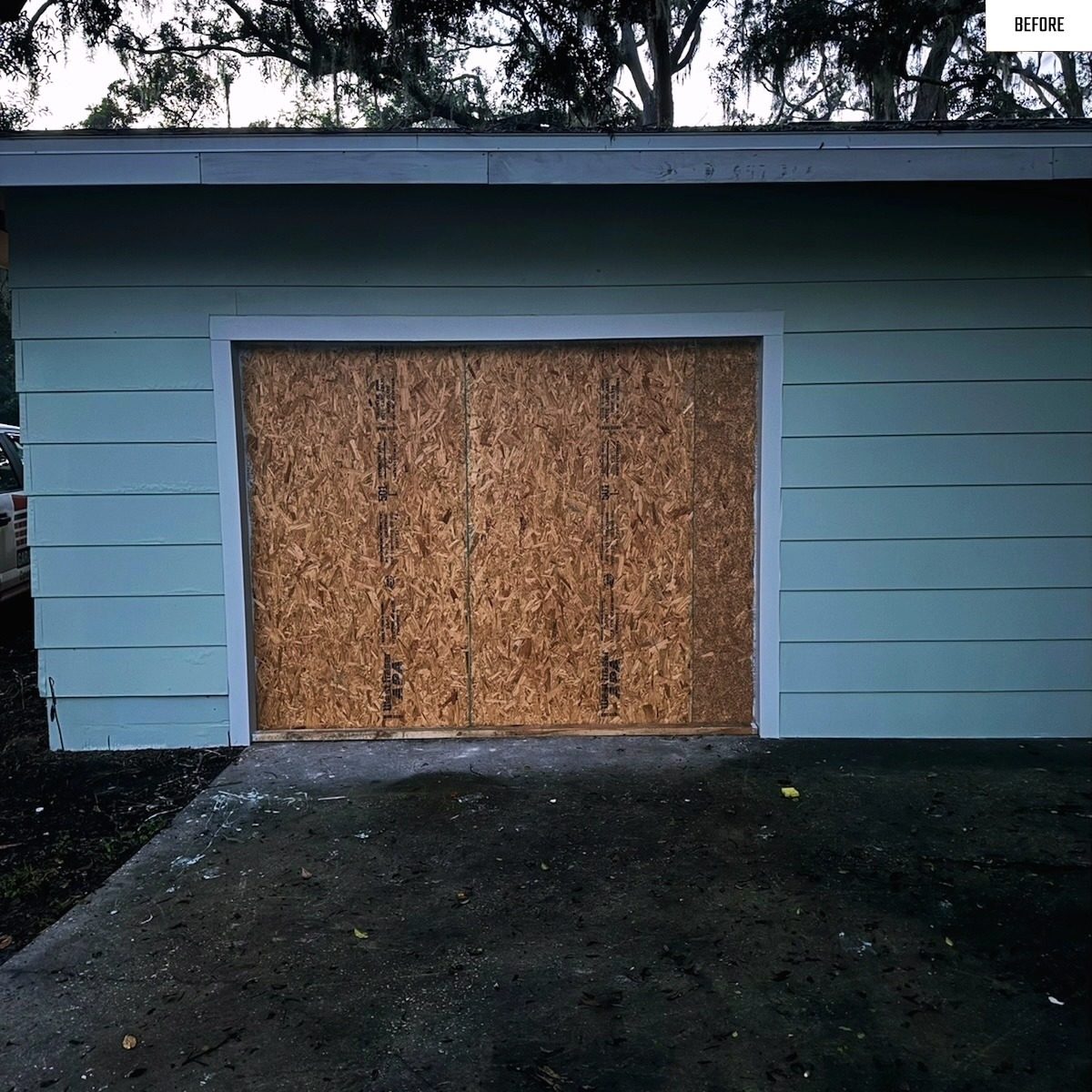 Before: boarded up garage opening replaced with a finished white door