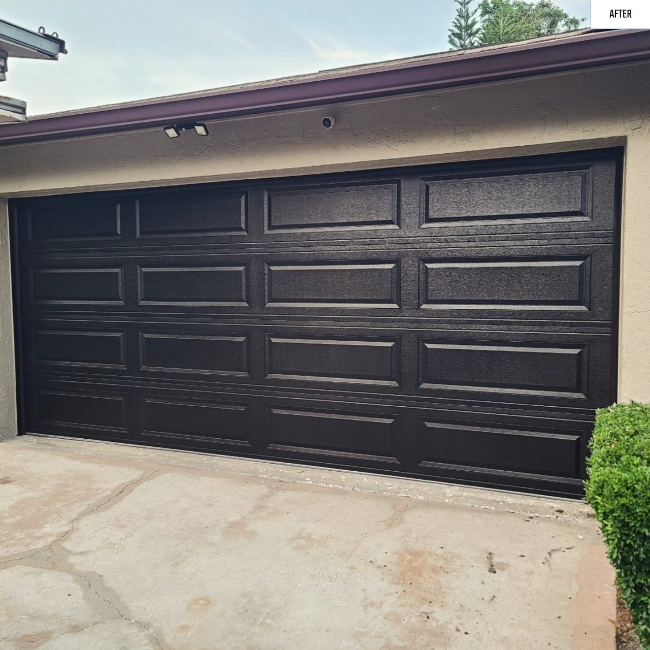 A black long panel garage door framed by shrubs