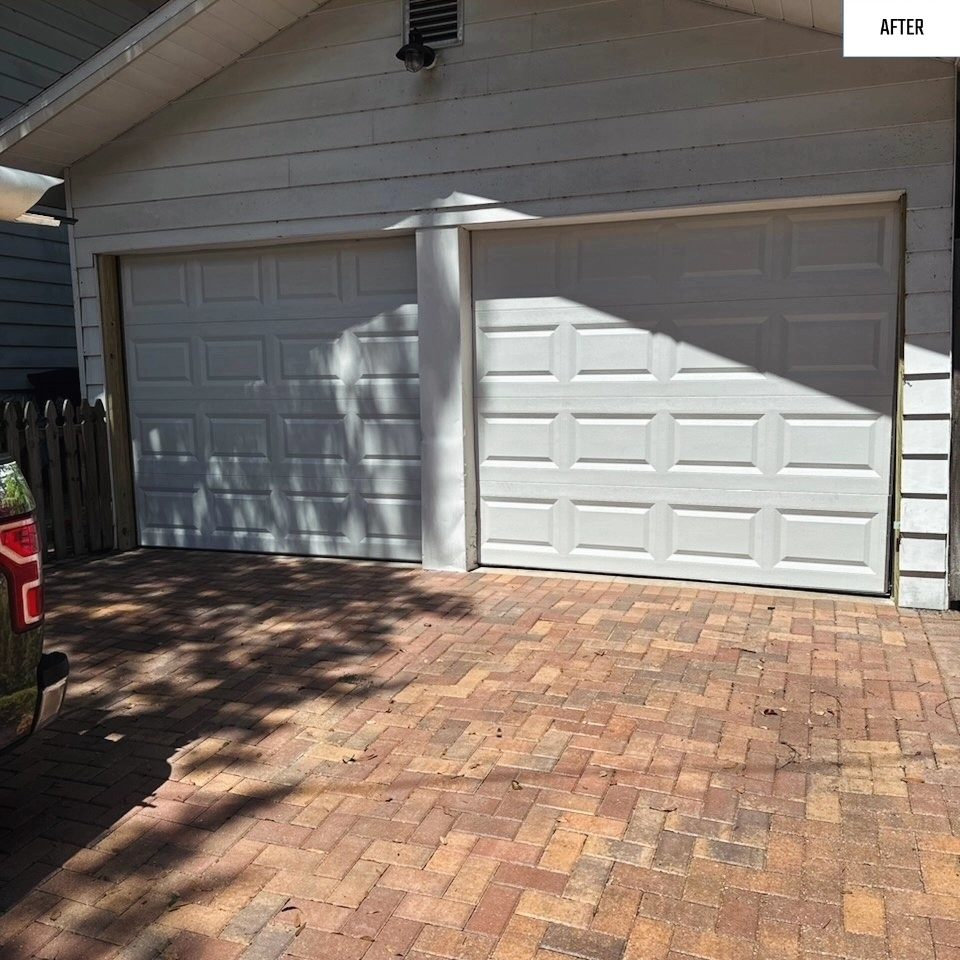 Two white garage doors on a home with a brick paver driveway